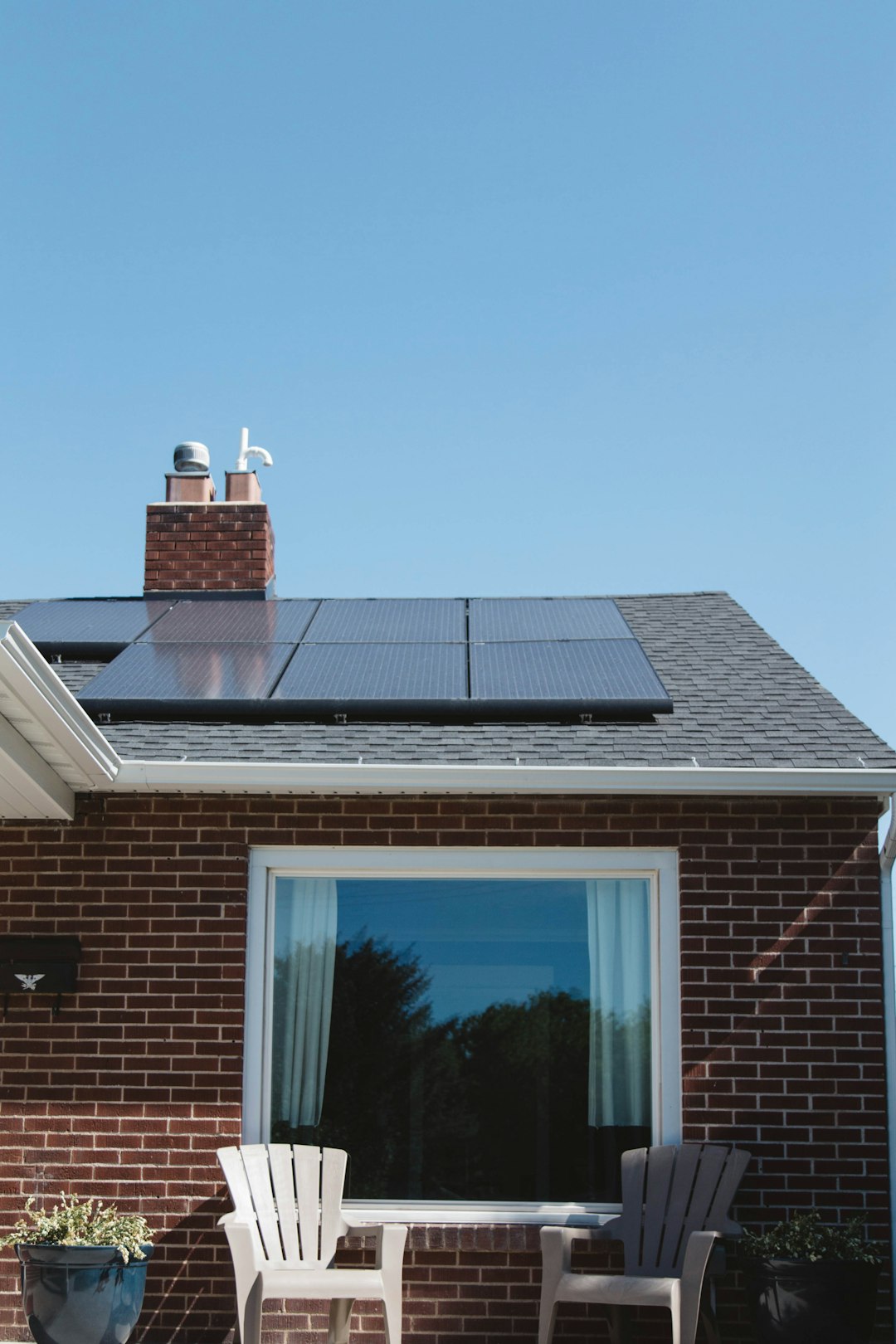 Home Vivint Solar - Solar Panels on roof of brick home with window and Adirondack chairs.